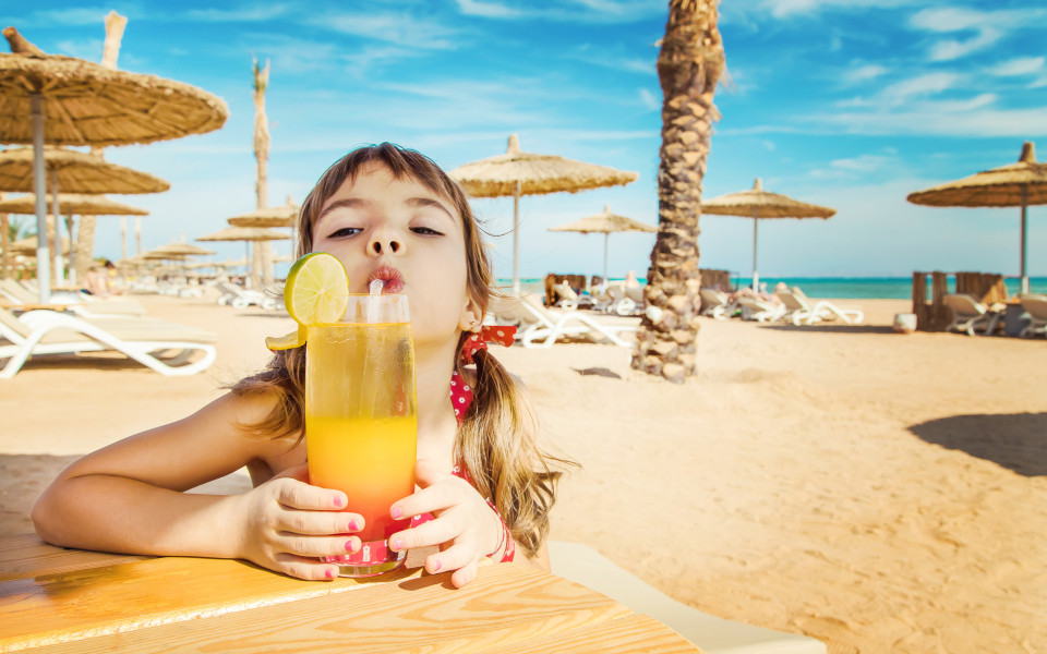 Kind am Strand mit Cocktail auf einer Strandliege